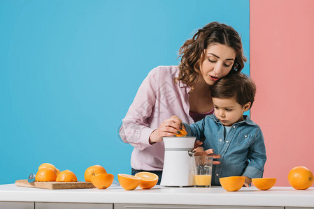 可爱的小可爱男孩妈挤压新鲜橙汁在果汁机图片
