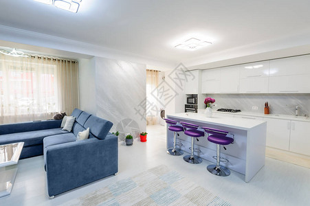 现代工作室公寓内有白色厨房和沙发紫色酒吧椅最图片