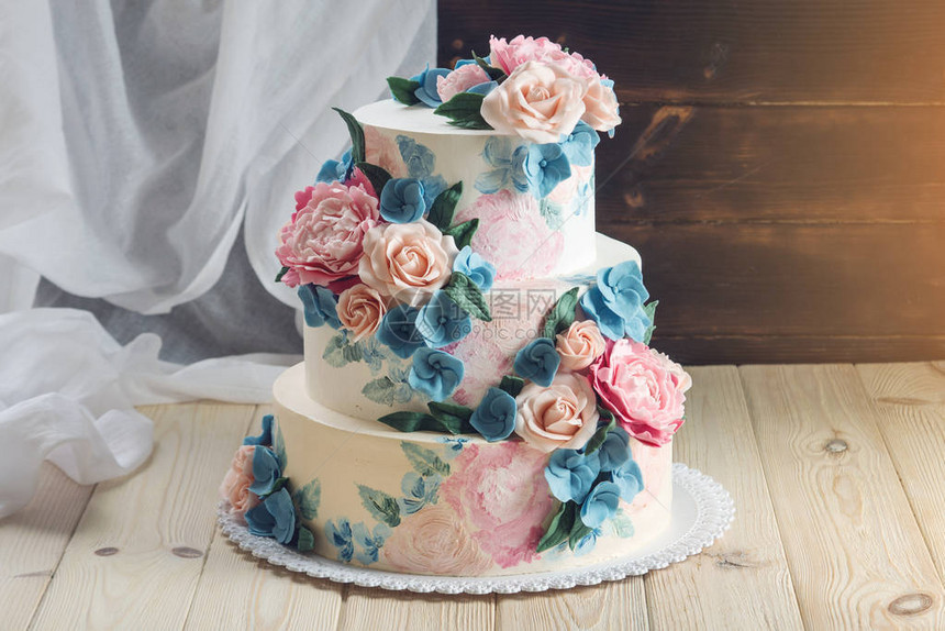 一个美丽的家庭婚礼三层蛋糕装饰着粉红玫瑰和蓝花在木制背景图片