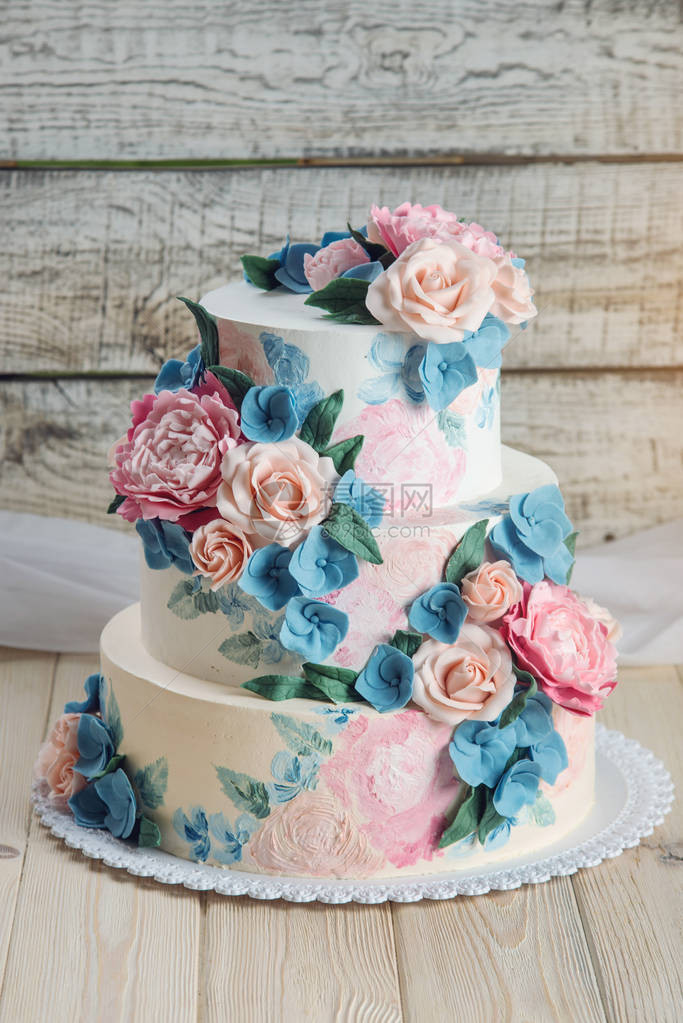 一个美丽的婚礼三层蛋糕装饰着粉红玫瑰和蓝花在木制背景图片