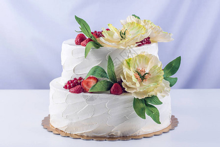 一个美丽的婚礼双层蛋糕上面装饰着花冠草莓和黄花还有绿色的叶子生图片