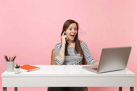 年轻兴奋的女人戴着耳机听音乐打视频电话坐在办公室工作图片