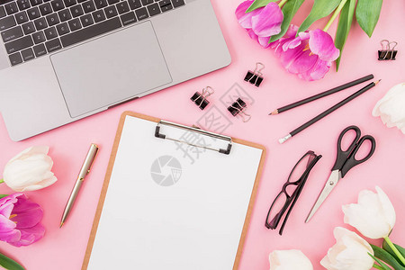 粉红色背景的笔记本电脑剪贴板郁金香花眼镜和饰品图片