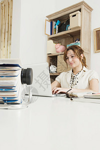 年轻有吸引力的职业商妇女利用一台笔记本电脑坐在她家办公室的白桌旁图片
