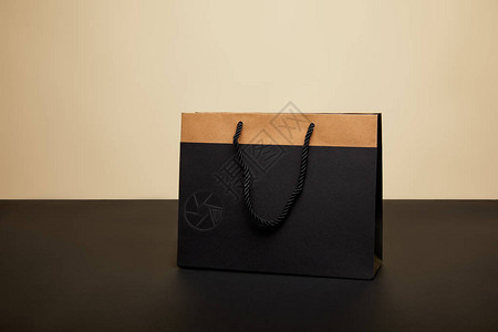 黑桌上一个黑购物袋在米色上隔背景图片