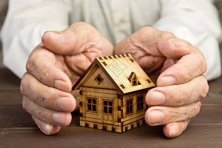 老人用手保护房屋模型风险保抵押贷款和银行贷款的概念贫图片