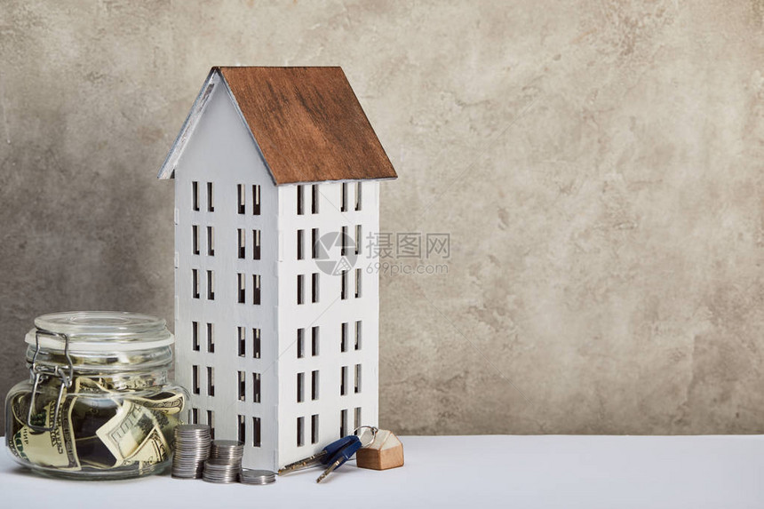 房屋模型用美元钞票钥匙和银币装在灰色背景白桌上的货币箱图片