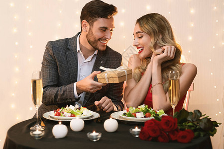 快乐的男人在餐厅的浪漫晚餐上给惊讶的女朋友送情人节礼物图片