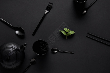 黑茶壶筷子各种勺子叉子杯子和薄荷叶在黑桌图片