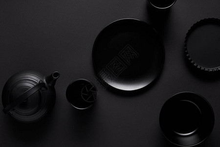 黑桌上的红茶壶盘子碗杯子和烤盘的顶视图背景图片