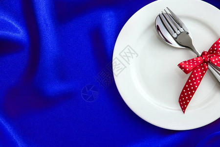 豪华蓝丝织物上带叉勺和红丝带的白色空图片