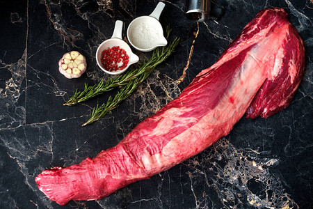 在大理石桌上的新鲜牛肉鲜嫩小菜配有调味料和迷迭香图片