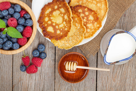 覆盆子蓝莓牛奶和蜂蜜糖浆煎饼在木桌上图片