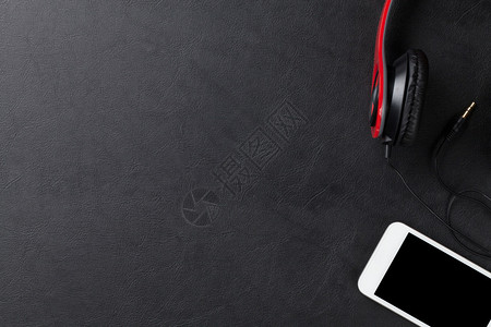 黑皮革桌上的耳机和智能手机顶视图背景图片