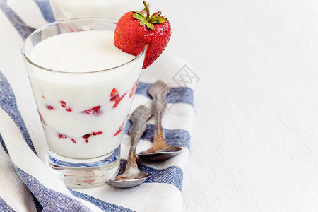 在白色背景的蓝色条纹餐巾纸上的玻璃杯中放置甜点酸奶和草莓层图片
