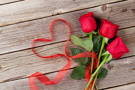 木桌上的红玫瑰和心形丝带图片