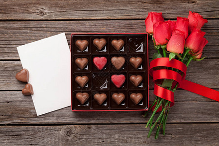 情人节贺卡与红玫瑰和心巧克力盒木制的桌子上带图片