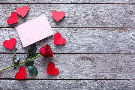 情人节背景与红玫瑰花和手工纸心和灰色质朴的木头上的空贺卡背景图片