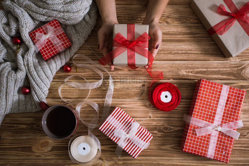 女用手把圣诞礼物包装在纸上用红白线和图片