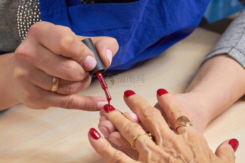 女人将红色清漆涂在指甲上美容院美甲师用红色清漆画女图片