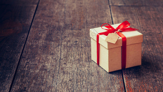 棕色礼品盒和红丝带与木背景与空间上的标签木板上的老式礼品盒图片