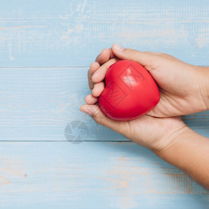 顶端握着红心形状的手在蓝糊色木背景上医疗器官捐赠和保险或爱与情人图片