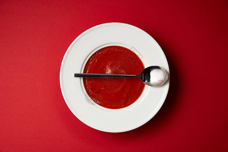 红桌上的盘子和勺子番茄汤的顶部视图图片
