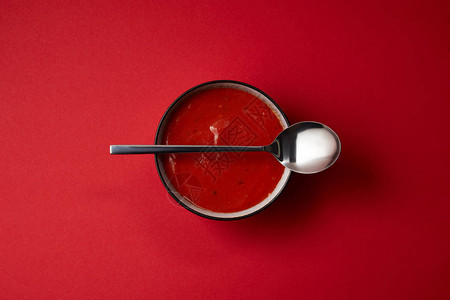 红桌上的盘子和勺子中美味的红番茄汤的顶部视图图片