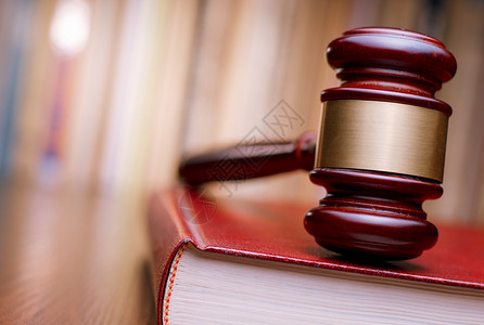 法官的木槌放在法庭桌子上的一本大红色法律书籍上背景图片