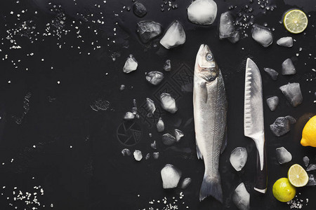 生鲈鱼用冰和刀在黑色背景海鲜餐厅或鱼市场的简约模型顶视图片
