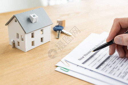 房屋经销商拿着笔靠近带有新房贷款字母房屋模型和钥匙的文图片