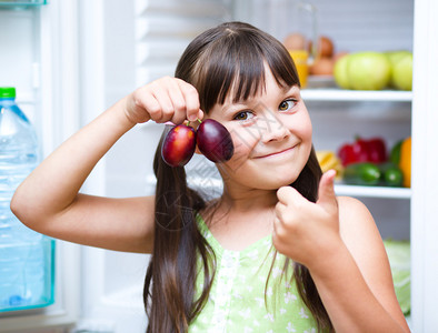 快乐的女孩在冰箱附近吃着水果蔬菜图片