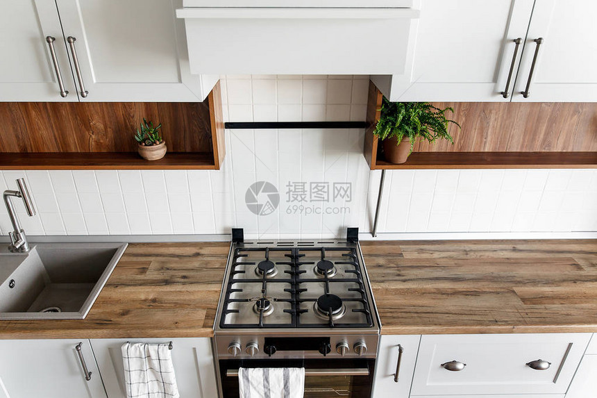 时尚的浅灰色厨房内部配有现代橱柜和新家的不锈钢器具斯堪的纳维亚风格的设计绿色植物装饰木制台面图片