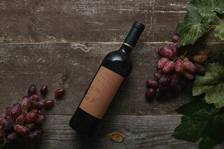 红酒瓶顶面有空白标签和新鲜成熟葡萄木制图片