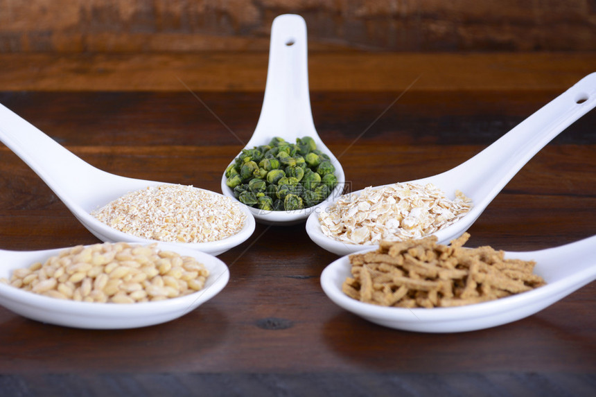 质朴的深色木桌上的勺子中的健康高纤维益生元谷物图片