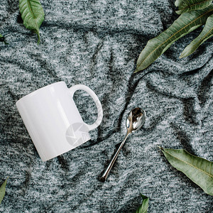 白杯勺子和灰色纺织品背景绿叶的空白模板平底面图片