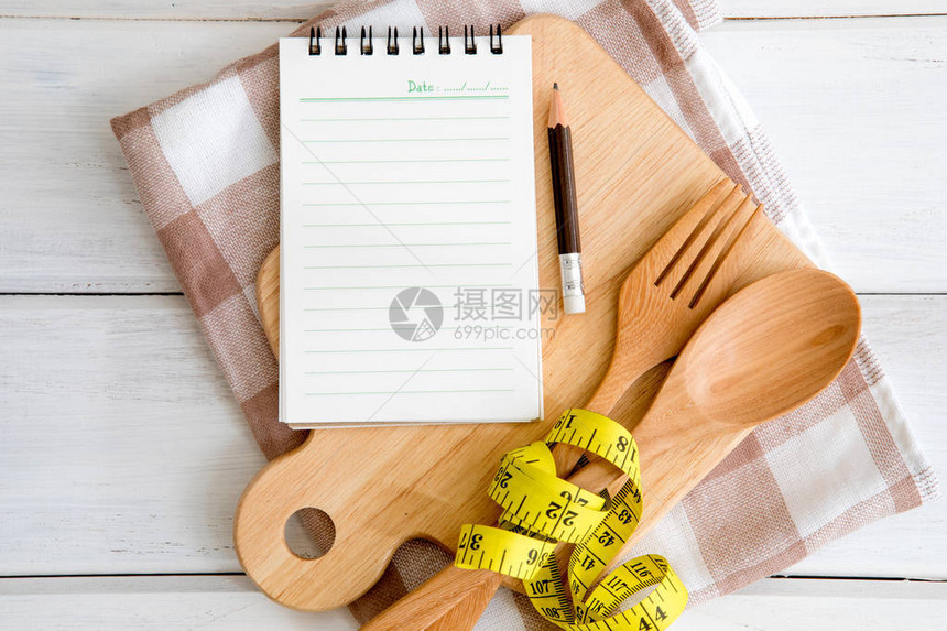 砧板上的记事本用木叉和勺子和白桌上的卷尺食谱物或健康习惯的饮食计划拍摄图片