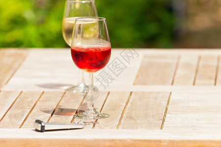 在木制花园桌边配有酒店钥匙的玫瑰酒杯图片