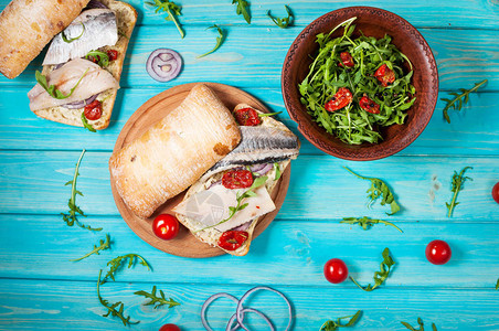蓝色木桌上的鲱鱼三明治和芝麻菜沙拉顶视图图片