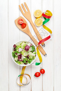 白色木制桌子上的新鲜健康沙拉用具和磁带测量图片