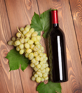 红葡萄酒瓶和一束白葡萄在木桌背景图片