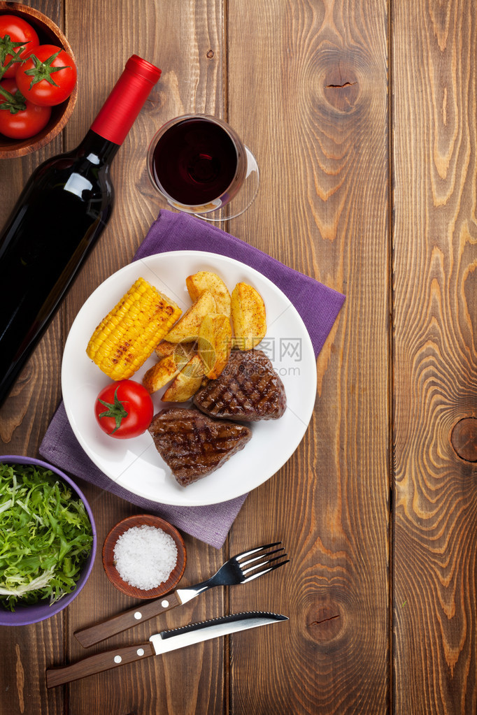 木桌上的牛排配烤土豆玉米沙拉和红酒图片