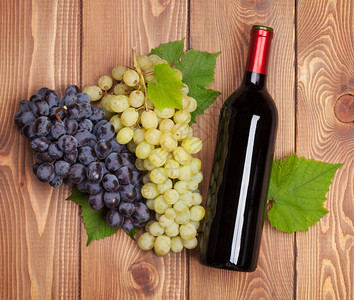 木桌背景上的红酒瓶和葡萄串图片