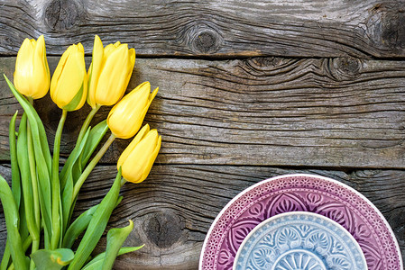 新鲜的黄色郁金香花与古老的盘子木制的桌子上图片