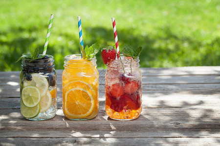 在花园木制桌边的玻璃罐子上配有夏季水果和浆果图片