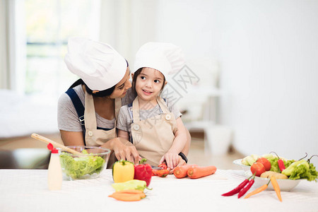 可爱的小女孩和她妈戴着厨师帽正在切菜做图片