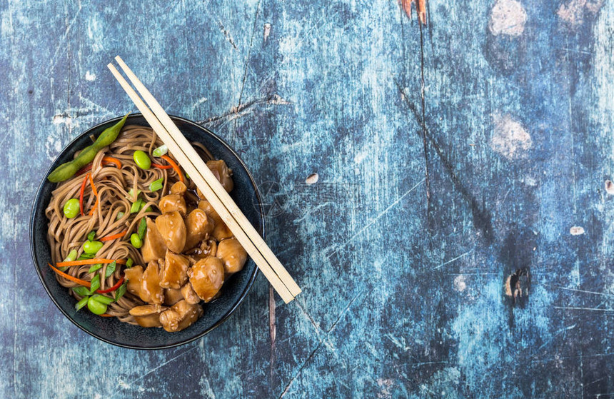 亚洲面条配鸡肉蔬菜碗质朴的木制蓝色背景文本的空间顶视图荞麦面照烧鸡肉毛豆筷子亚洲风味晚餐中图片