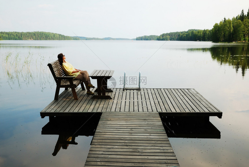 女人坐在木制扶手椅上她正在宁静的湖边的板图片
