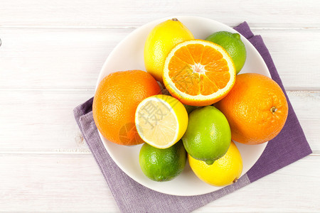 盘子上的柑橘类水果橙子酸橙和柠檬在木桌背景上图片