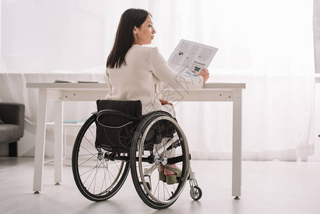 在工作场所坐在轮椅上时持有报纸的年轻残疾女青年商图片